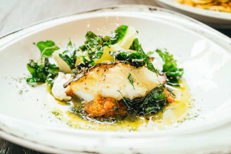 A traditional Ligurian-style baked salt cod with potatoes, olives, and pine nuts, garnished with fresh parsley.