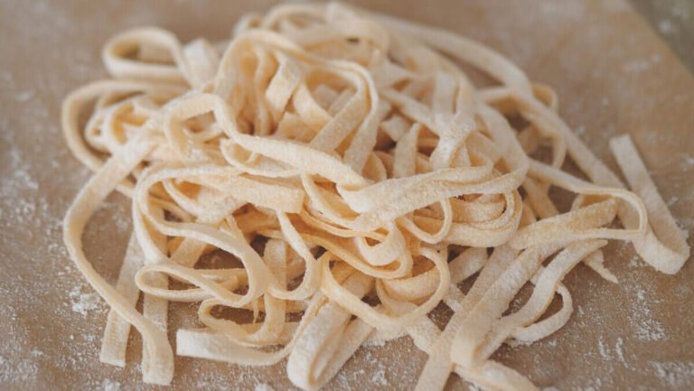 Homemade tagliatelle pasta on wooden board with flour and rolling pin